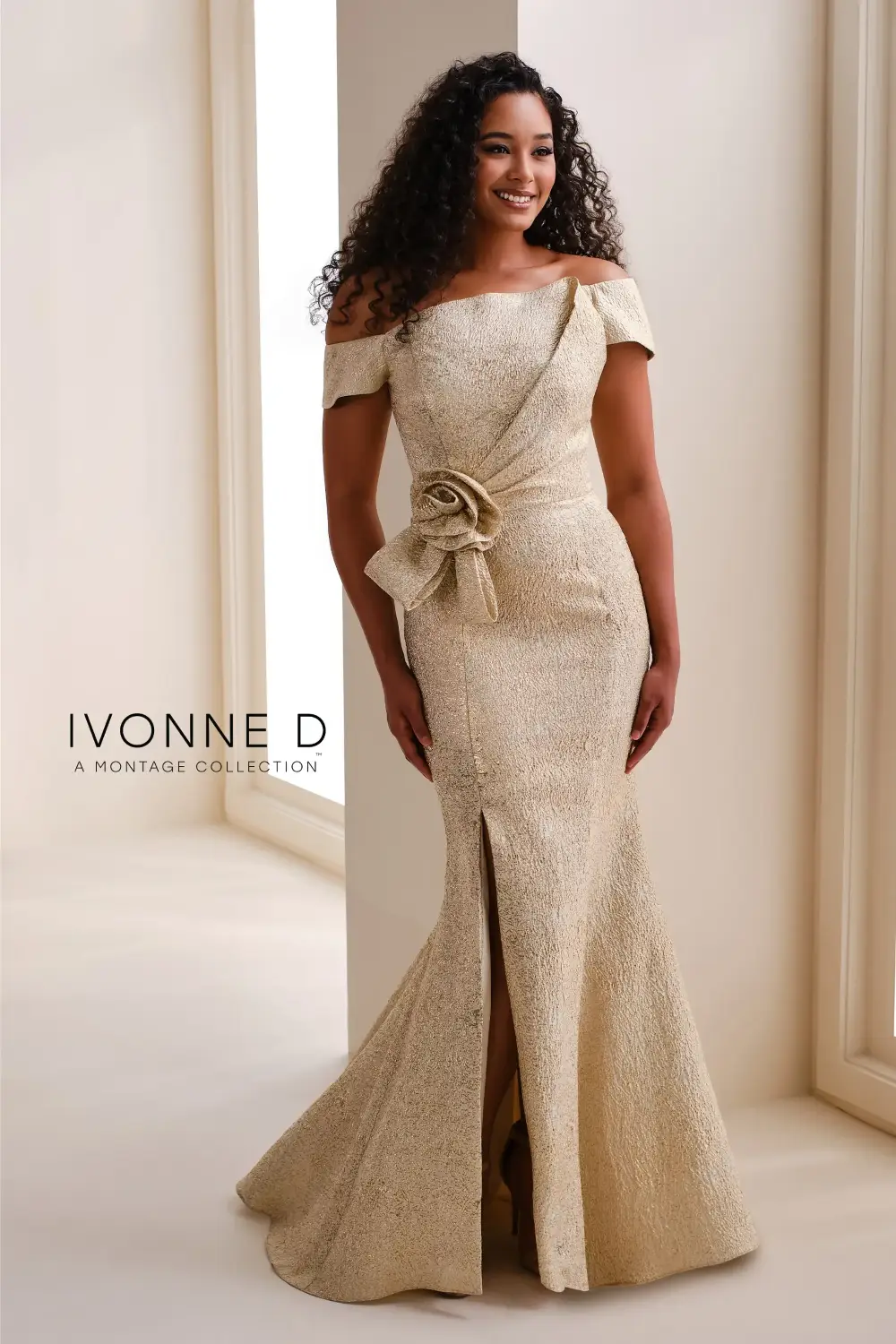 A woman wearing an elegant off-the-shoulder gown with a fitted silhouette and a decorative ribbon detail at the waist, posing in a well-lit setting.