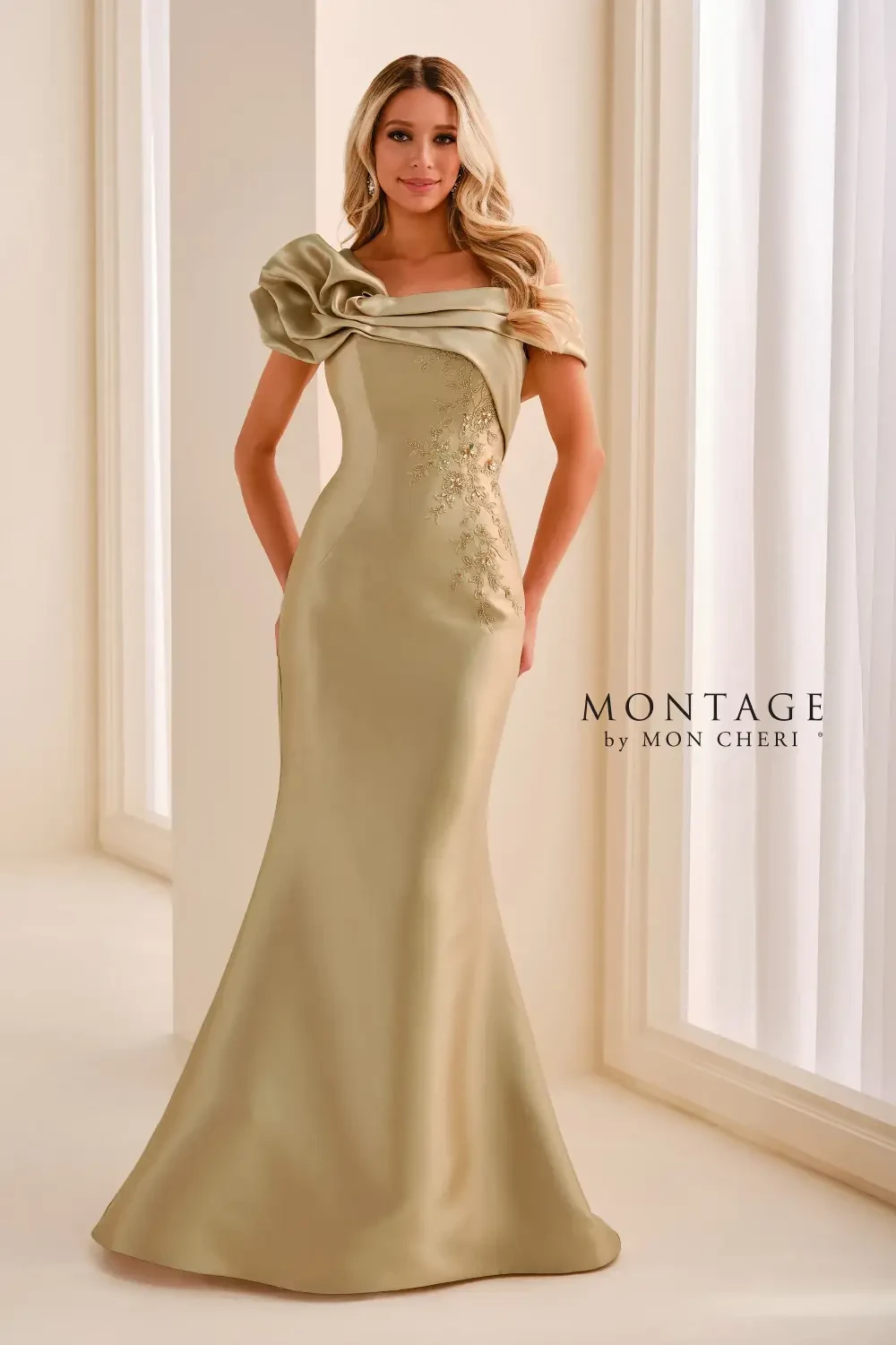 A woman wearing a sophisticated, elegant beige dress with a one-shoulder design and a floral accent. The dress has a fitted silhouette and flares out towards the bottom.
