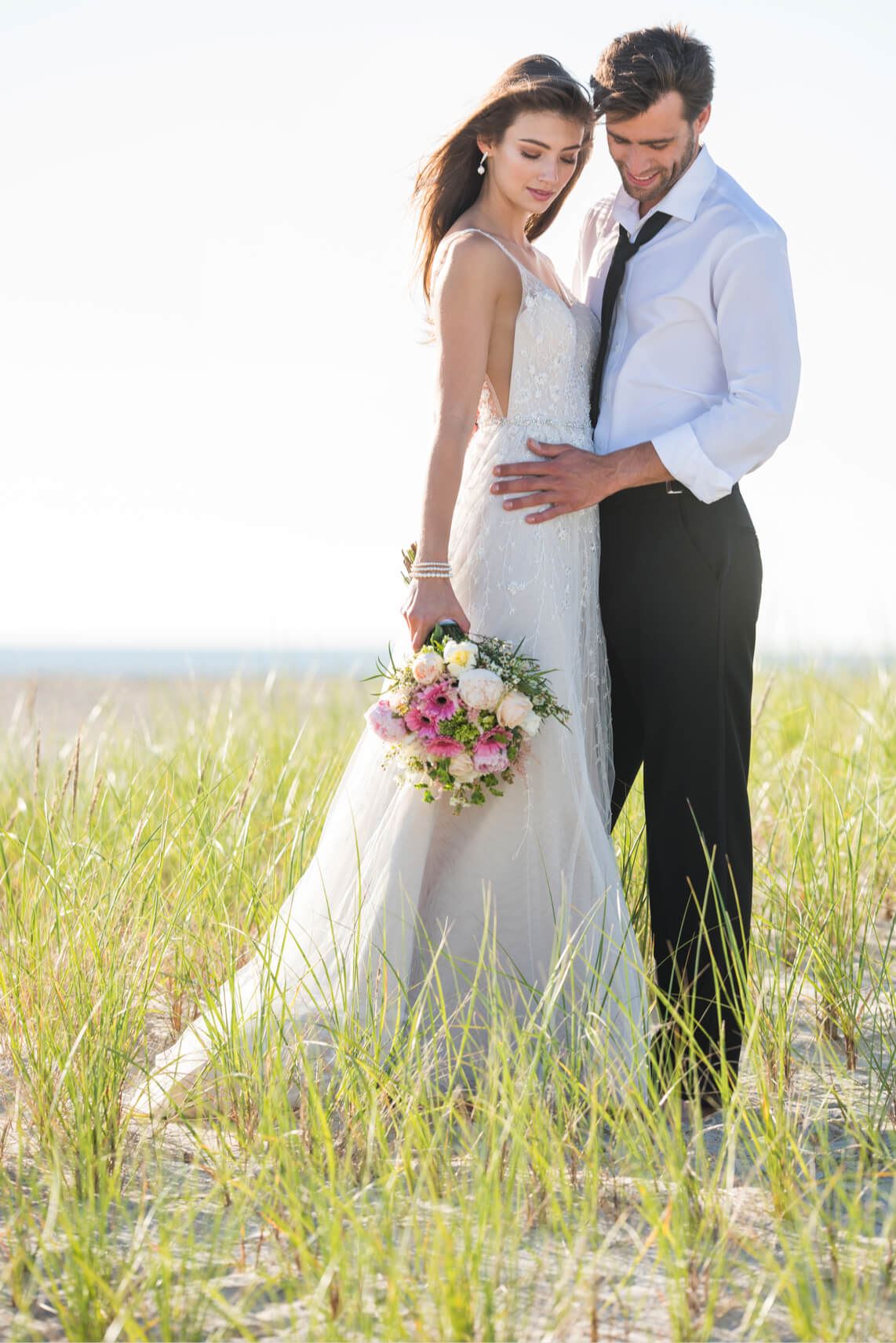Brunette bride and groom holding each other in field